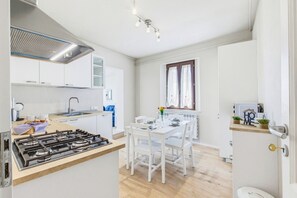 A modern kitchen with a gas stove, white cabinets, and a dining area with a white table and chairs. - Rosa Olivi - Lavaiano (Lavaiano)
