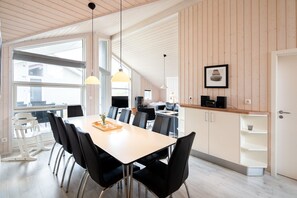 A modern kitchen with a dining area, wooden paneling, and a large window. - Coastal Wellness House fur 10 Personen (Grossenbrode)