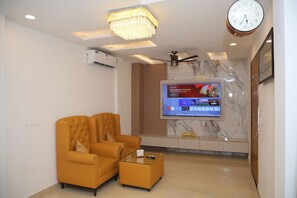 A modern living room with a sofa, coffee table, TV, air conditioning unit, ceiling fan, and a clock on the wall.