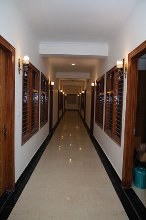 A long, narrow hallway with wooden doors and wall sconces, leading to a room with a ceiling fan.