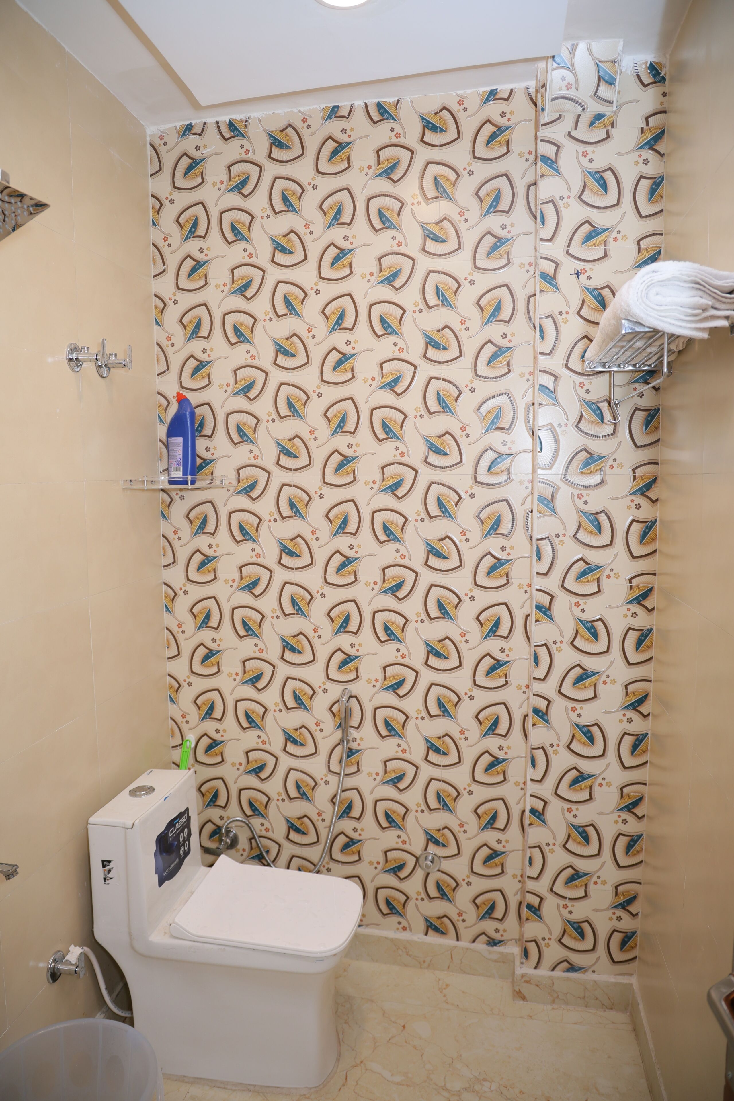 A bathroom with a shower curtain featuring a leaf pattern, a toilet, a sink, and a towel rack.