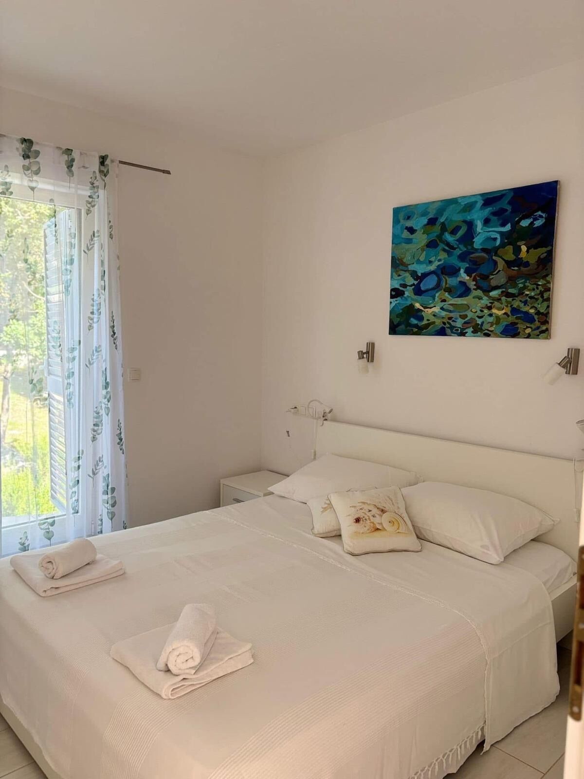 Une chambre à coucher avec un lit, des oreillers, un tableau et une fenêtre avec des rideaux.