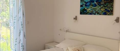 A bedroom with a bed, pillows, a painting, and a window with curtains.