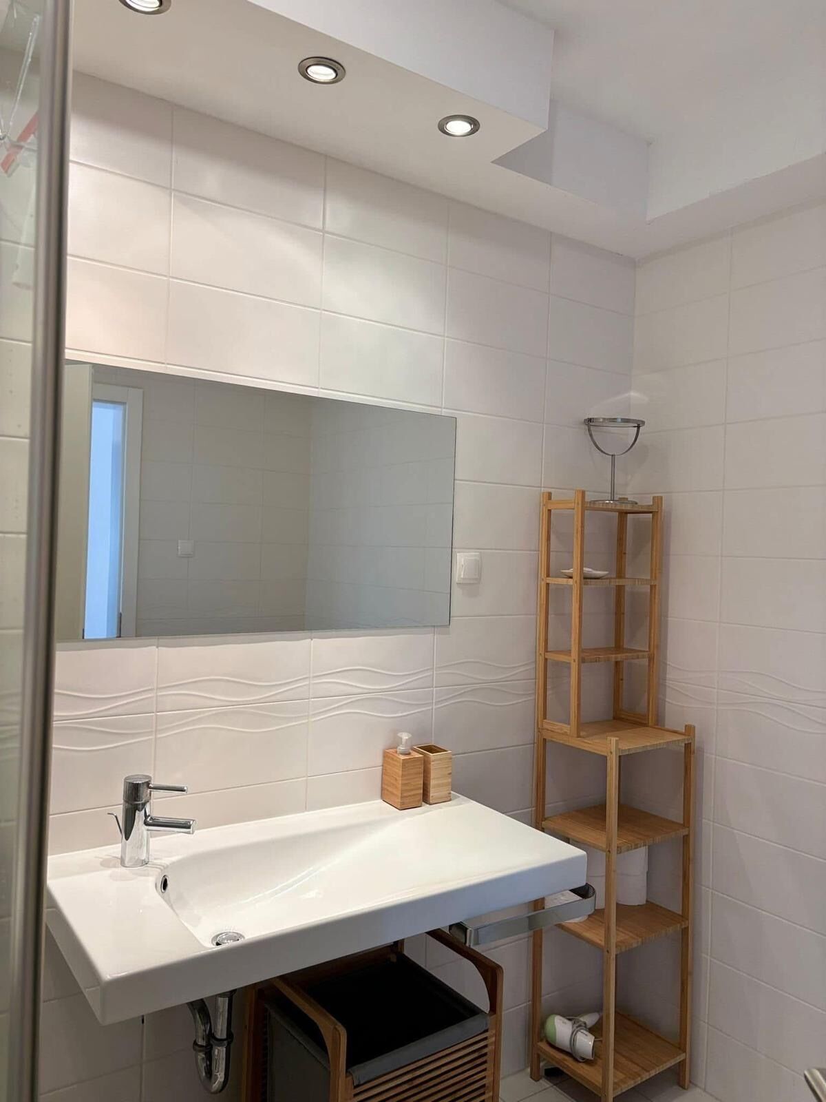A bathroom with a white sink, a mirror, and a wooden shelf unit.