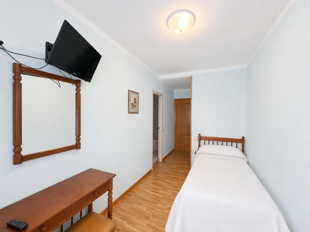Een slaapkamer met een bed, een bureau, een aan de muur bevestigde televisie en een deur naar een andere kamer.