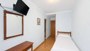 Een slaapkamer met een bed, een bureau, een aan de muur bevestigde televisie en een deur naar een andere kamer.