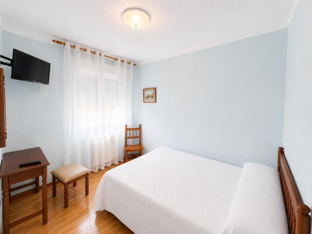 Un dormitorio con cama, escritorio, silla, televisor y un cuadro en la pared.