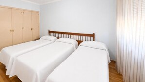 Una habitación con dos camas individuales, cabecera de madera, armario y ventana con cortinas.