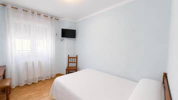 Una habitación con cama, una silla, un televisor montado en la pared y un ventanal con cortinas.