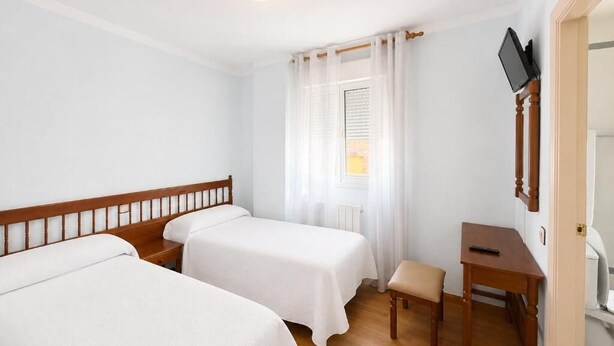 Habitación de hotel con dos camas individuales, un escritorio de madera, una silla y un televisor en la pared.