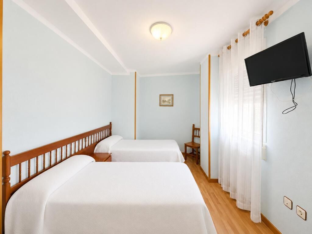 Habitación de hotel con dos camas, un televisor montado en la pared y un ventanal con cortinas.