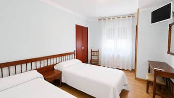 Una habitación de hotel con dos camas individuales, un escritorio de madera, un televisor y una ventana con cortinas.
