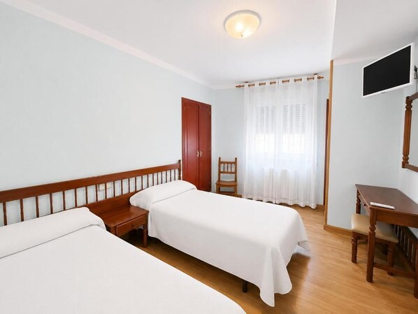 A hotel room with two single beds, a wooden desk, a television, and a window with curtains.
