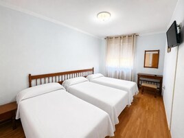 A room with two single beds, a wooden bench, a television, and a window with curtains.