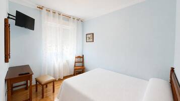 Ein Hotelzimmer mit Bett, Schreibtisch, Stuhl, Fernseher und einem Fenster mit Vorhängen.