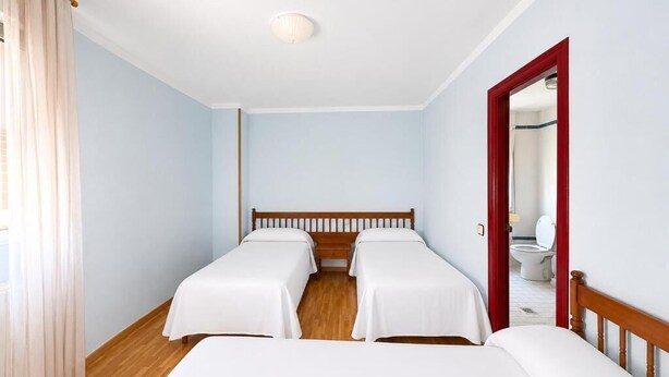 A hotel room with two single beds, wooden flooring, a white ceiling, and a red door.