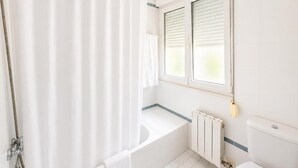 Un baño con bañera, inodoro, ventana con persianas y cortina de ducha.