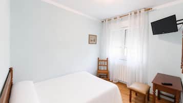 Ein Schlafzimmer mit einem Bett, einem Sessel, einem Schreibtisch, einem Fernseher und einem Fenster mit Vorhängen.
