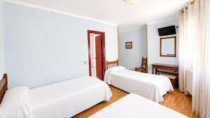A hotel room with two single beds, a wooden desk, a chair, a television, and a door leading to another room.