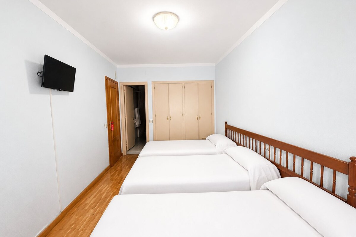 Habitación de hotel con dos camas, un televisor, un armario y una puerta que da a un baño.