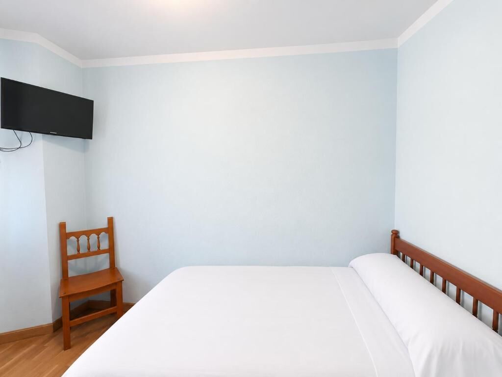 A bedroom with a bed, a wooden chair, and a flat-screen TV mounted on the wall.