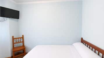 Un dormitorio con cama, una silla de madera y un televisor de pantalla plana montado en la pared.
