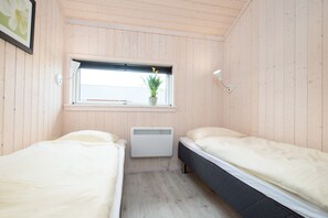 Ein kleines Zimmer mit zwei Betten, einem Fenster mit Pflanze, einem Heizkörper und einer Wandleuchte.