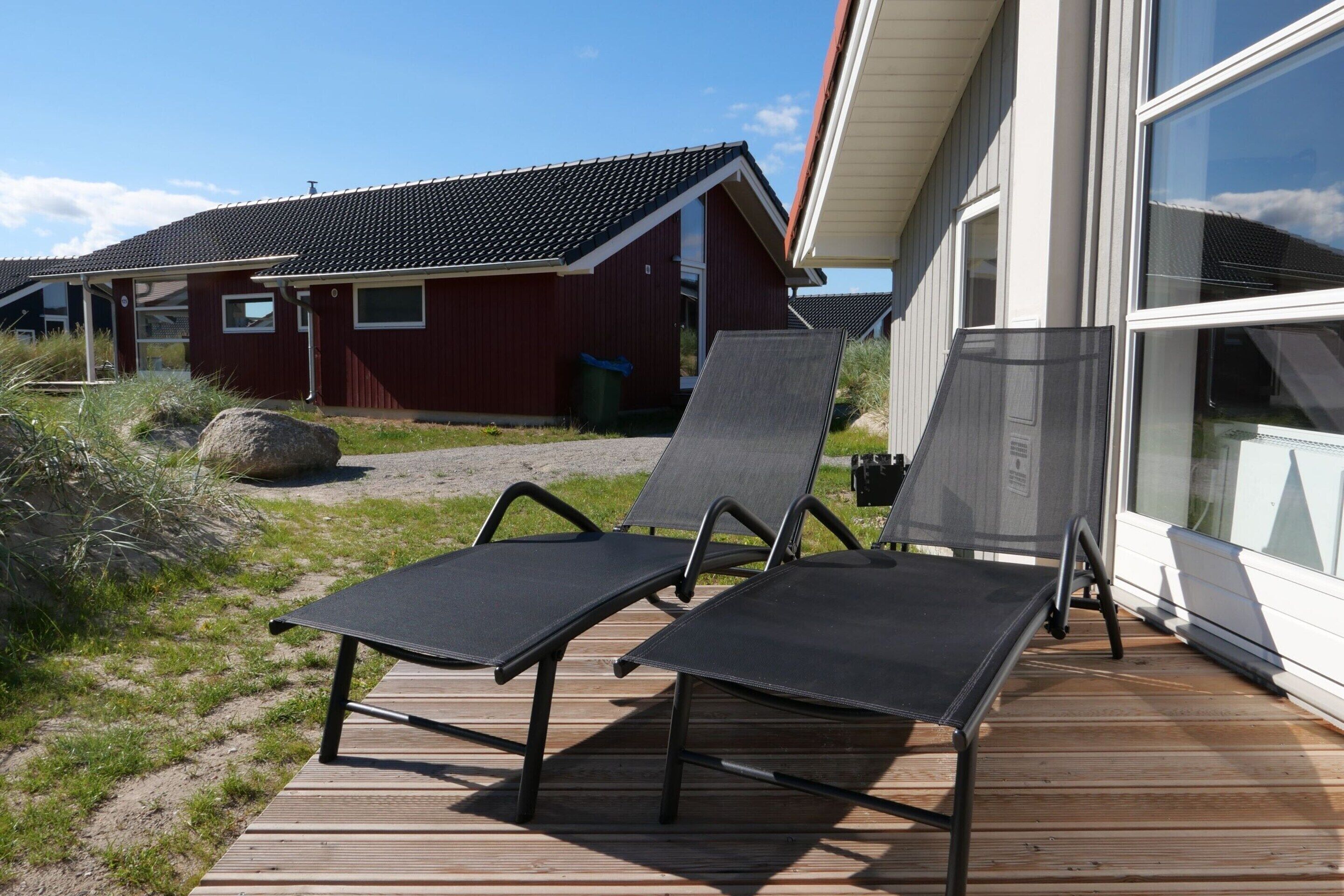 A wooden deck with two lounge chairs, a red building, and a large window.