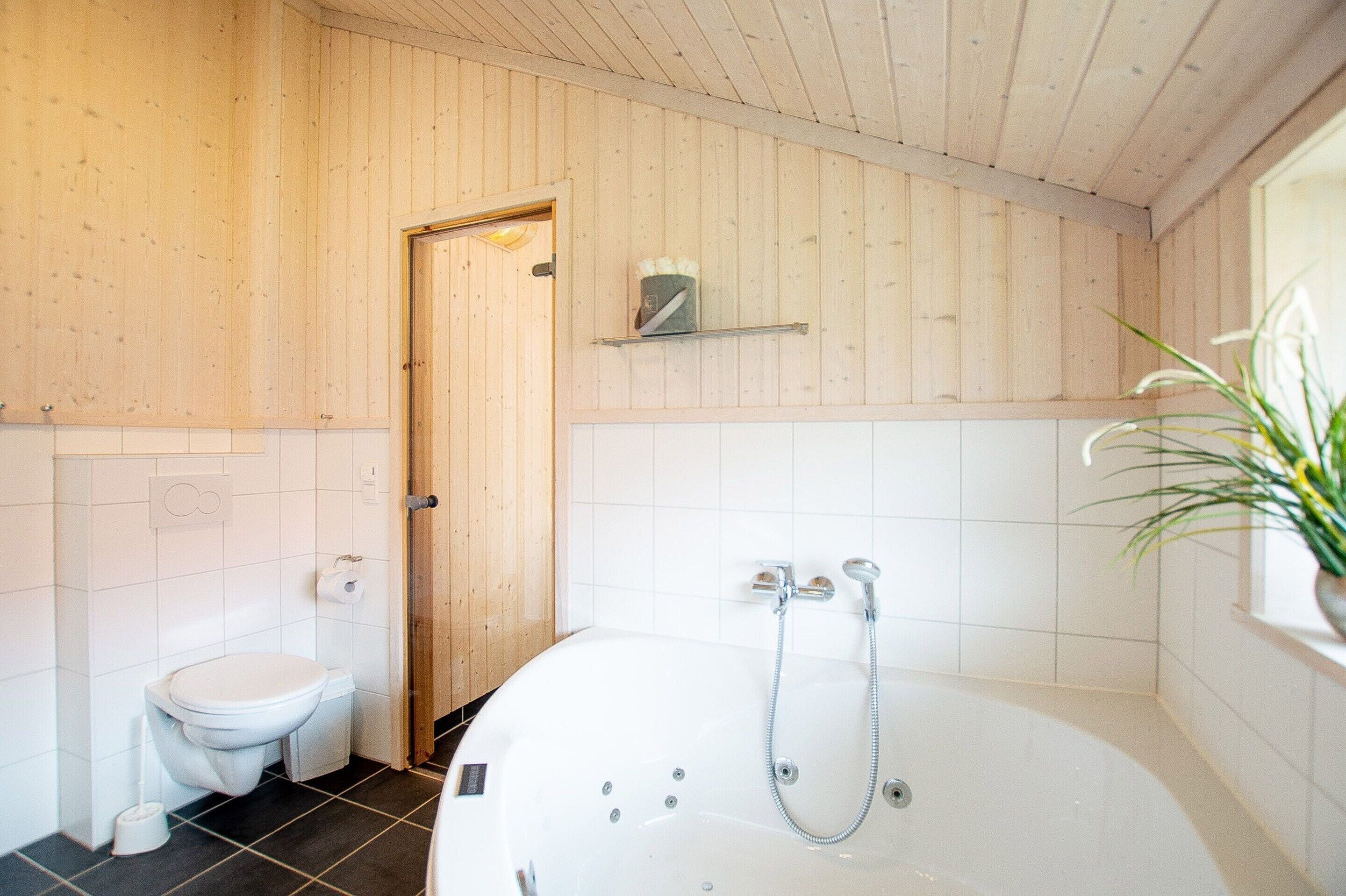 Een badkamer met houten inrichting, een witte badkuip, een toilet en een plank met een handdoek.