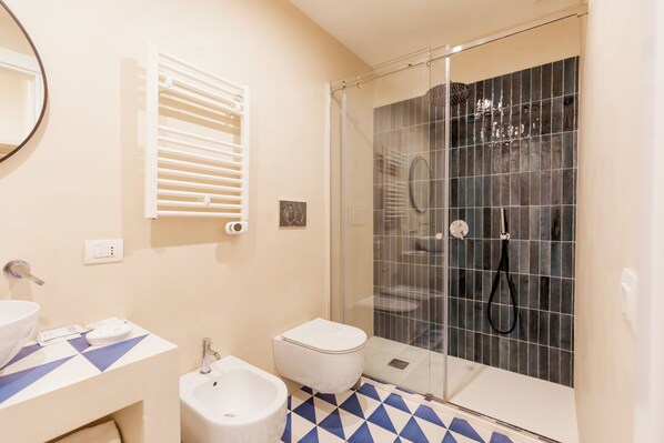 Ein Badezimmer mit einer Duschkabine, einem Bidet, einer Toilette und einem Waschbecken mit blau-weißer Fliesenrückwand.