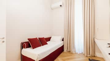 Quarto pequeno com uma cama de solteiro, cabeceira vermelha, roupa de cama branca e janela com cortinas bege.