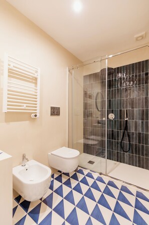 Ein Badezimmer mit Bidet, Toilette, einer Duschkabine und einem gemusterten Boden.
