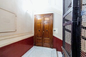 Um corredor com porta dupla de madeira, piso ladrilhado e parede vermelha.