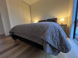 A bedroom with a bed, a nightstand, a lamp, and a window.
