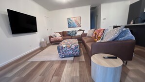 Un salon moderne comprenant un téléviseur à écran plat, un ensemble de canapés, un pouf et une table basse ronde.