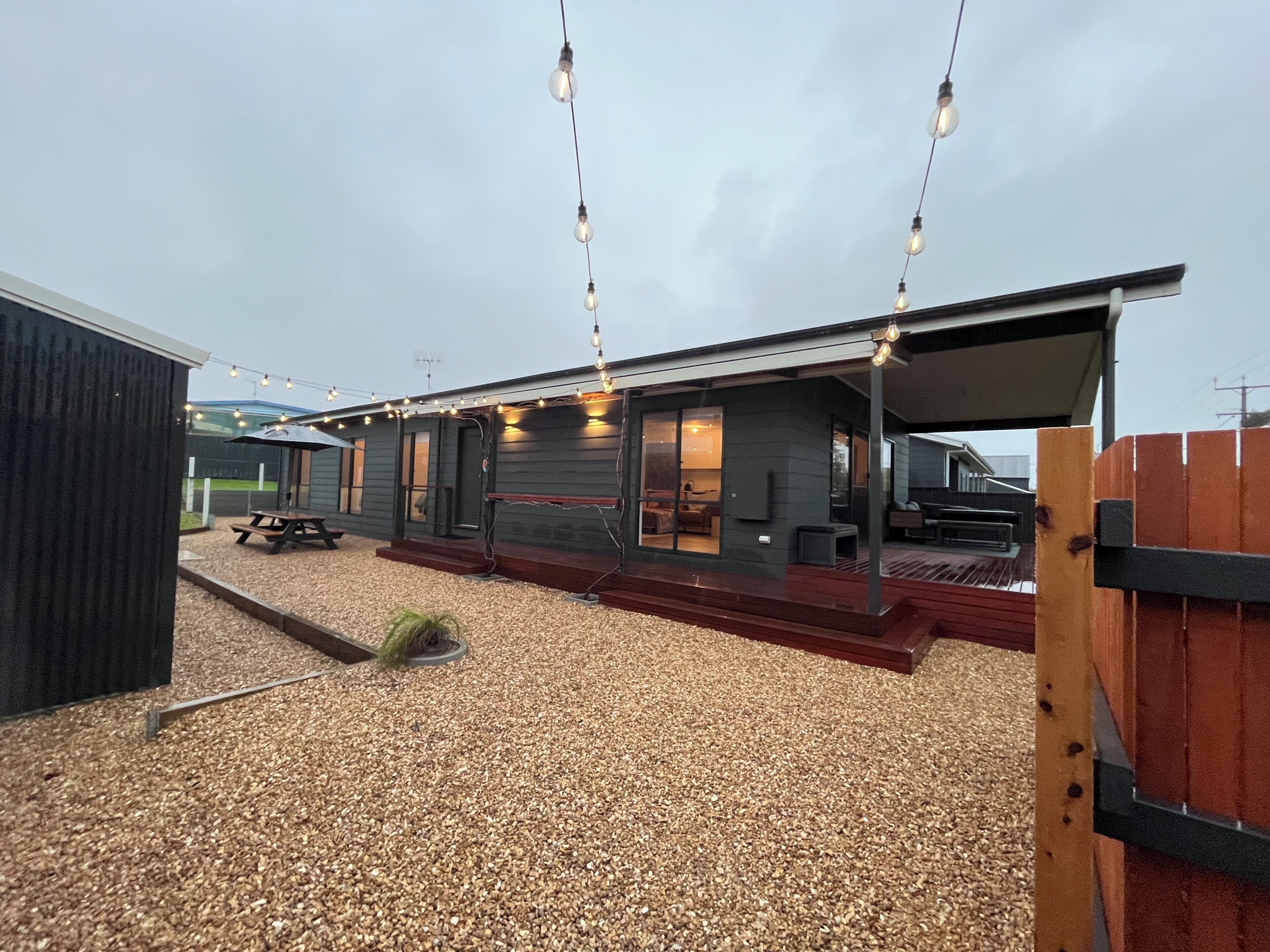 Een modern huis met een overdekt terras, zitplaatsen buiten en lichtjes.