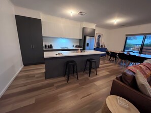 A modern kitchen with a central island, bar stools, and a dining area with a large window.