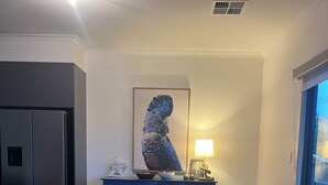 Un espace repas moderne avec une table en bois, des chaises noires, un luminaire central et une grande œuvre d’art encadrée accrochée au mur.