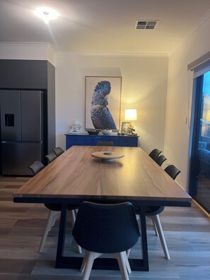 A modern dining area with a wooden table, black chairs, a central light fixture, and a large framed artwork on the wall.