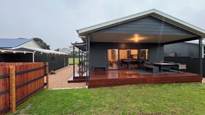 Un patio extérieur couvert comprenant un espace repas, un barbecue et une terrasse en bois.