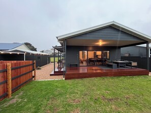 A covered outdoor patio with a dining area, a barbecue grill, and a wooden deck.