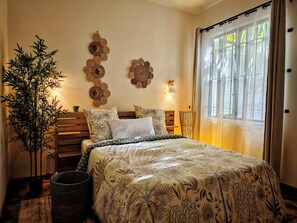 Ein Schlafzimmer mit einem Bett, einem Blumentopf, Wanddekoration und einem Fenster mit Vorhängen.