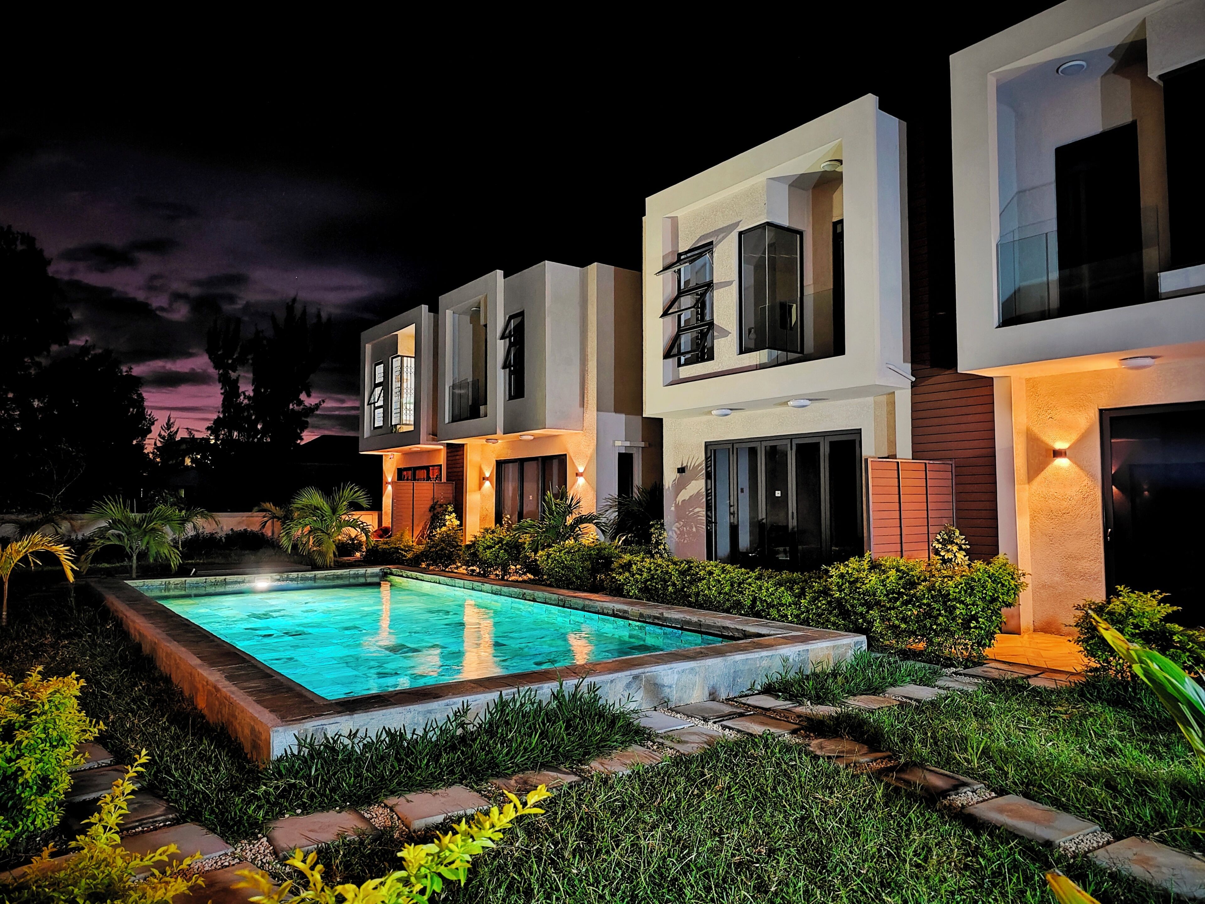 A modern two-story residential building with a swimming pool, surrounded by well-maintained landscaping.