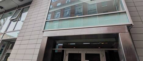 A modern building with a glass facade, a set of double doors, and a visible staircase leading to an upper level.