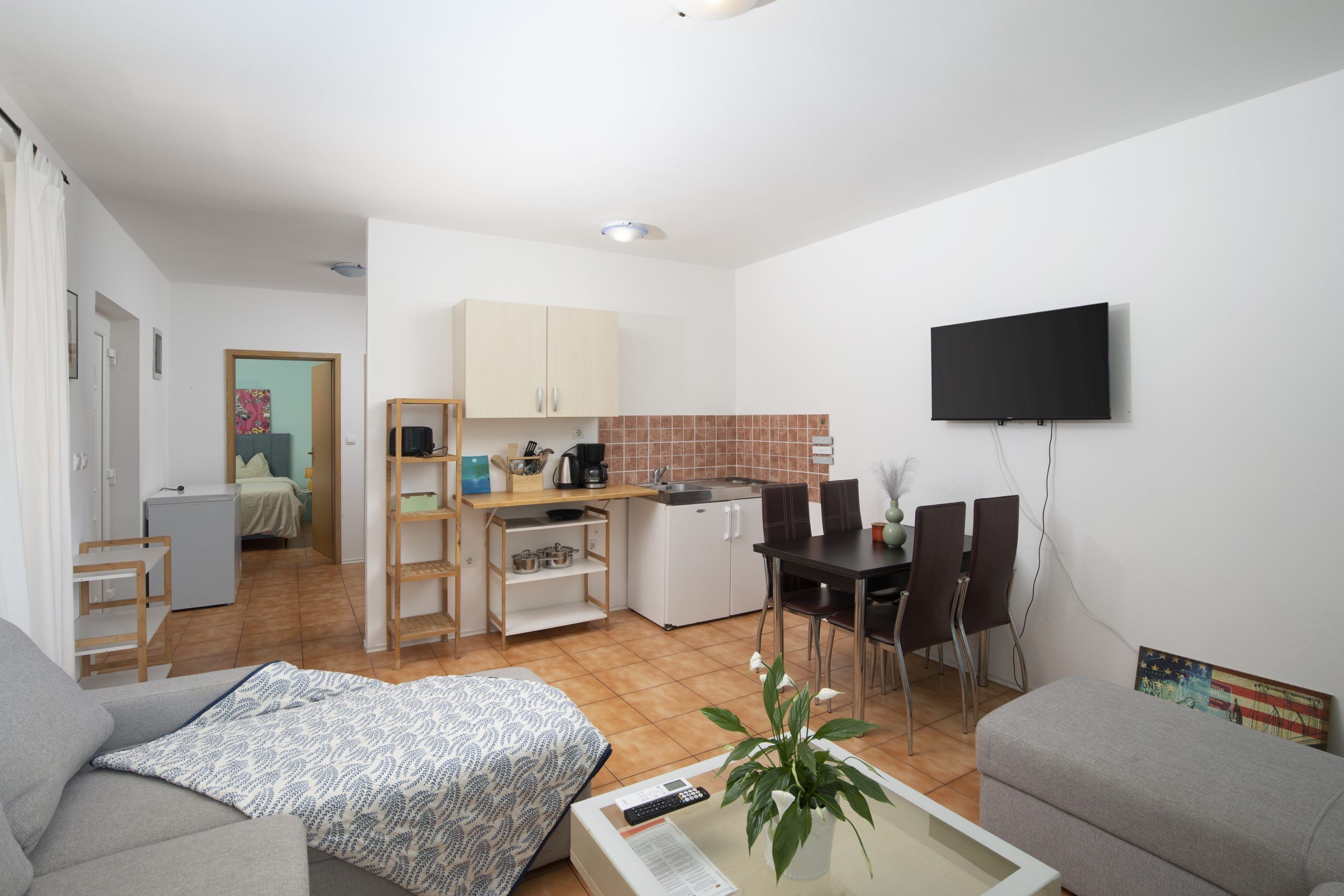A compact living space with a kitchenette, a dining area, and a seating area with a TV mounted on the wall.