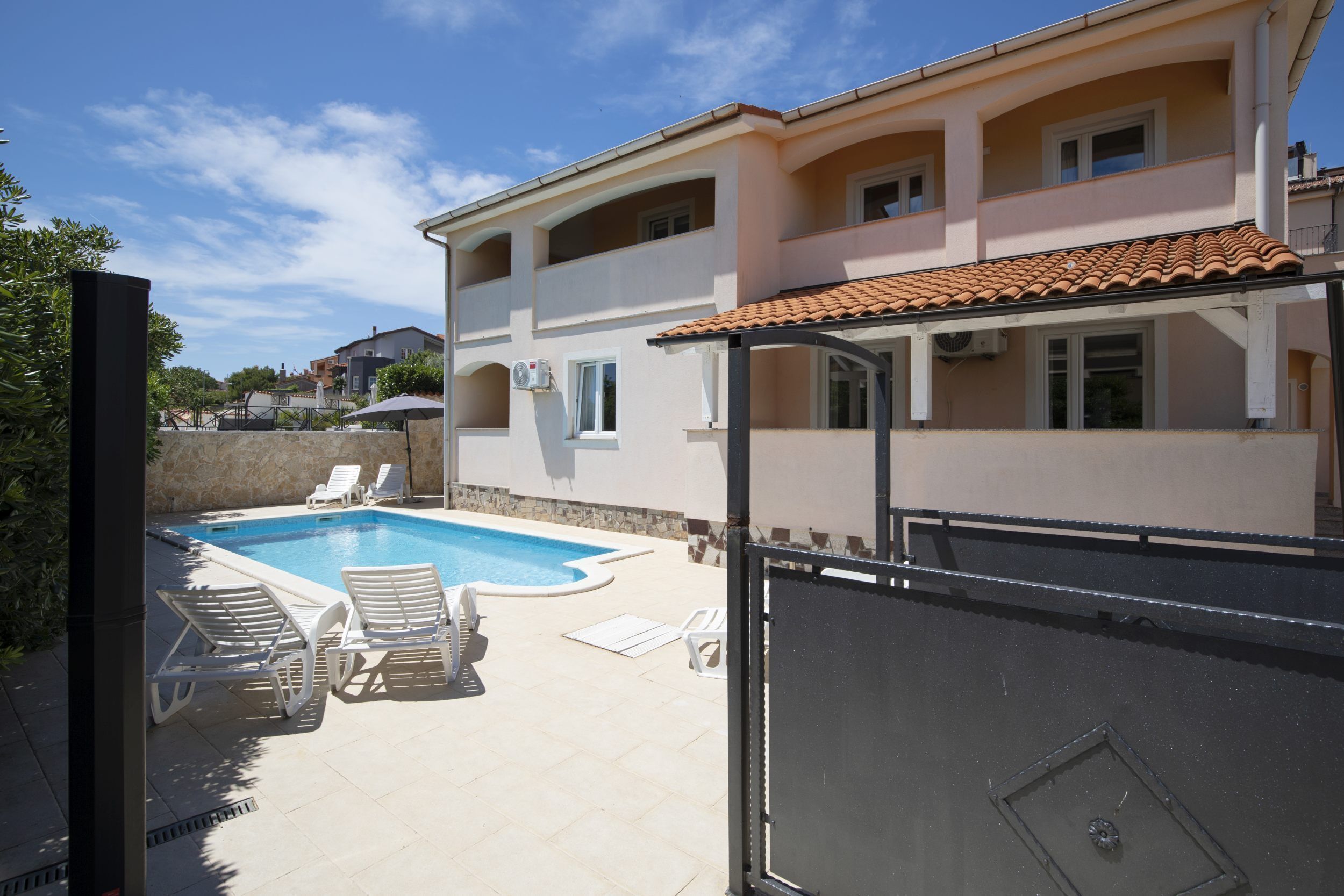 A two-story building with a swimming pool, outdoor seating, and a gated entrance.