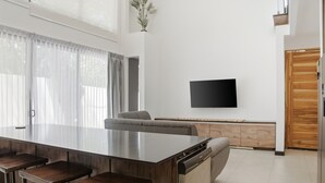 Et moderne køkken med en central ø, barstole, indbygget ovn og et fladskærms-tv på væggen.
