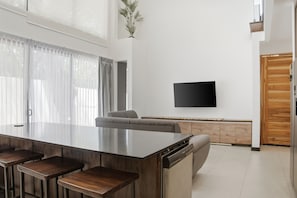 A modern kitchen with a central island, bar stools, a built-in oven, and a flat-screen TV mounted on the wall. - Brisas Tranquilas #1 is a private 2-bedroom, 2-bathroom retreat with a fully equipped kitchen, washer and dryer, private pool, and parking. Enjoy a peaceful and comfortable stay with everything you need for a relaxing getaway. (Playas Del Coco)