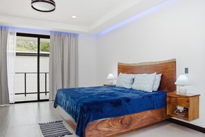 A bedroom with a bed, nightstands, a wooden headboard, a view through a glass door, and a window with curtains. - Brisas Tranquilas #1 is a private 2-bedroom, 2-bathroom retreat with a fully equipped kitchen, washer and dryer, private pool, and parking. Enjoy a peaceful and comfortable stay with everything you need for a relaxing getaway. (Playas Del Coco)