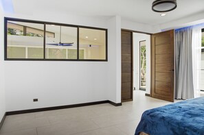 Une chambre avec une grande fenêtre, une porte donnant sur un balcon et un lit recouvert d’une couverture bleue.